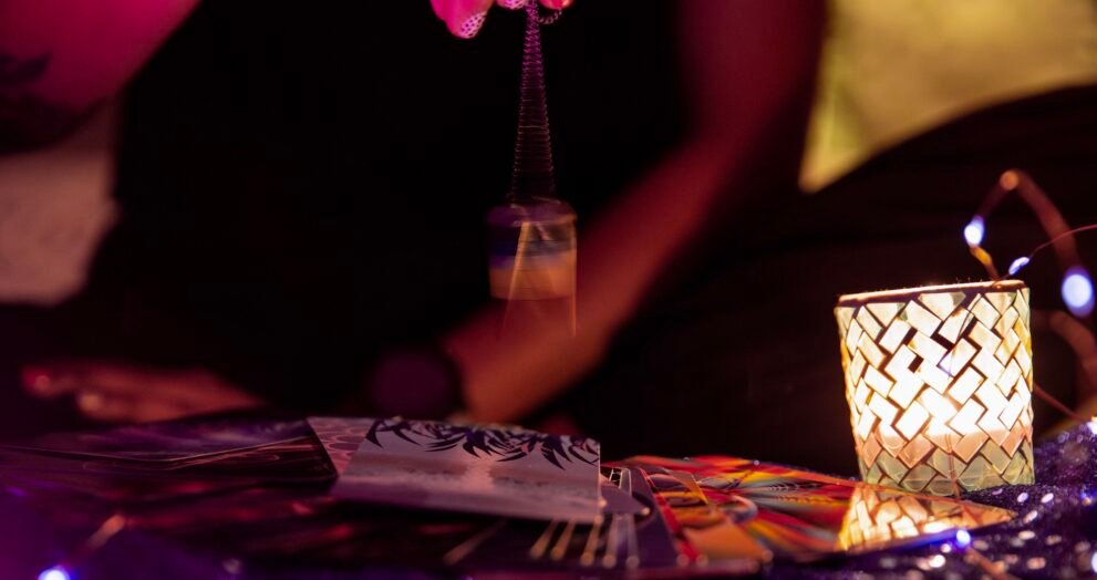 Main balançant un pendule au-dessus de cartes de tarot, avec une bougie allumée à côté.