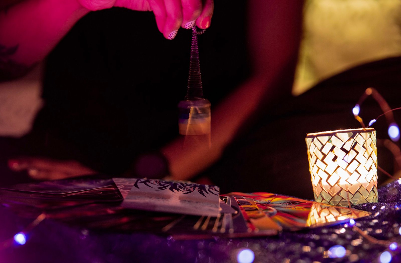 Main balançant un pendule au-dessus de cartes de tarot, avec une bougie allumée à côté.